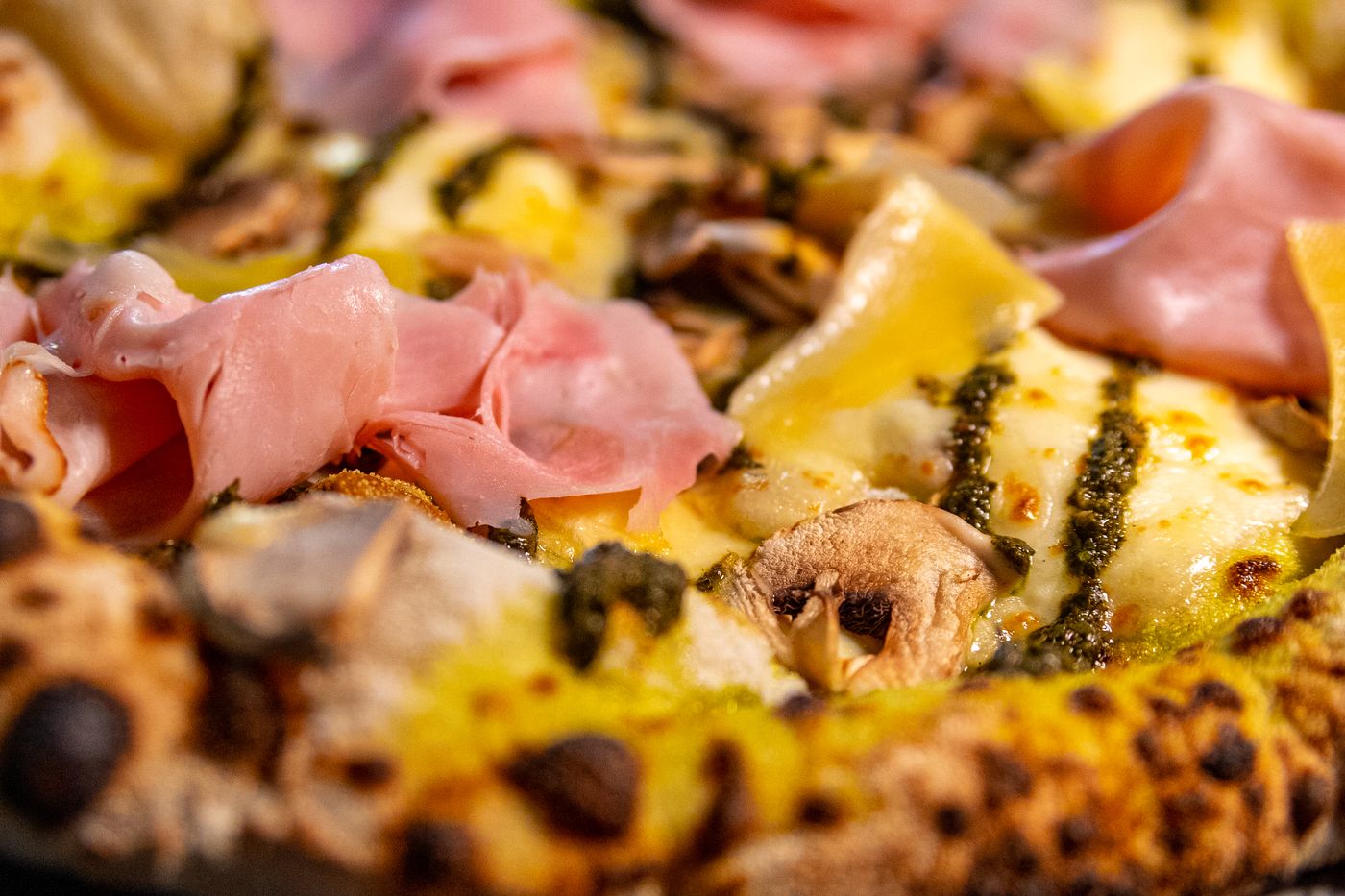Detalle de la corteza quemada y el queso de la pizza de jamón, pesto y champiñones