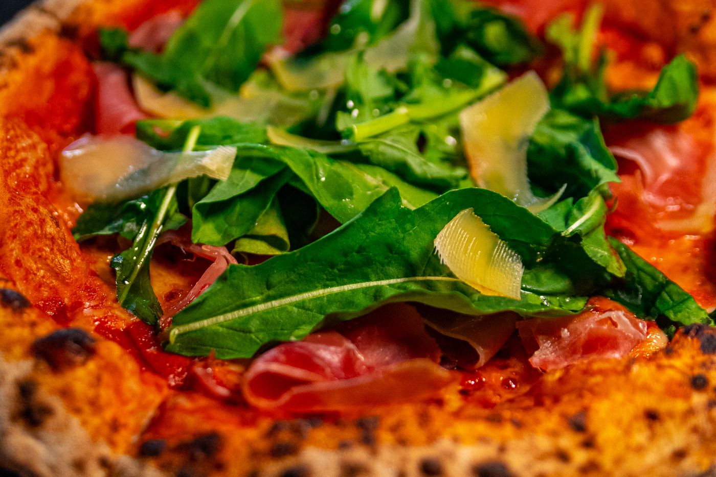 Detalle de la rúcula fresca y el prosciutto sobre la pizza recién horneada