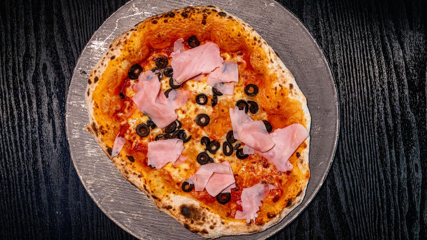 Pizza de jamón y aceitunas de masa madre sobre piedra, vista desde arriba